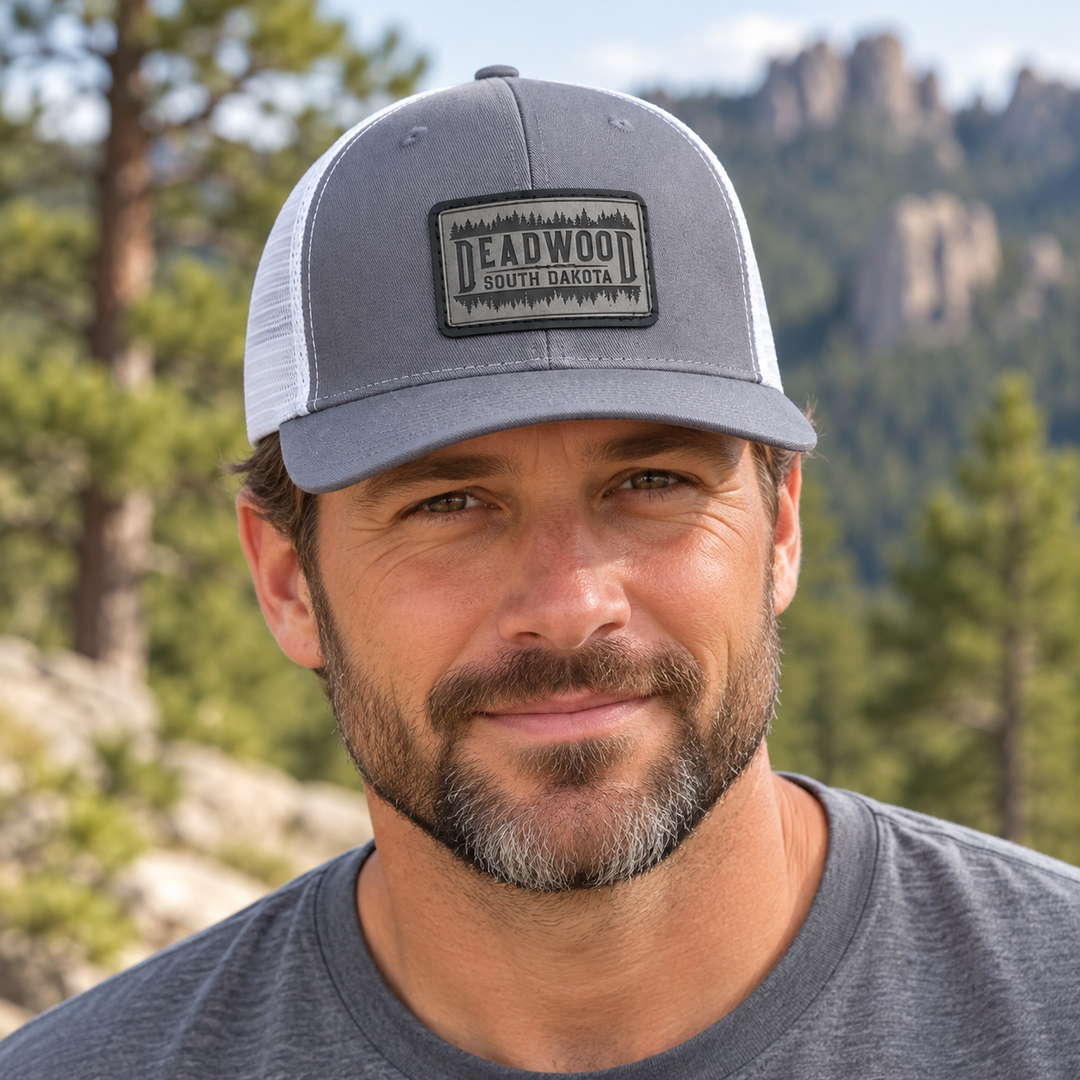 Male model wearing gray and white Deadwood South Dakota leather patch hat; AI-generated lifestyle image