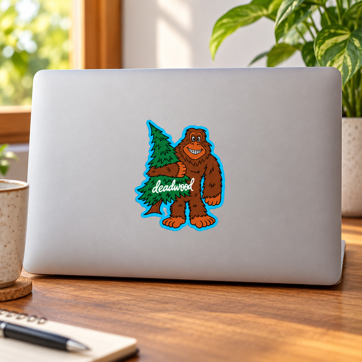 Deadwood Smiling Bigfoot Hugging a Pine Tree Sticker on a laptop — lifestyle display mockup; accessories not included